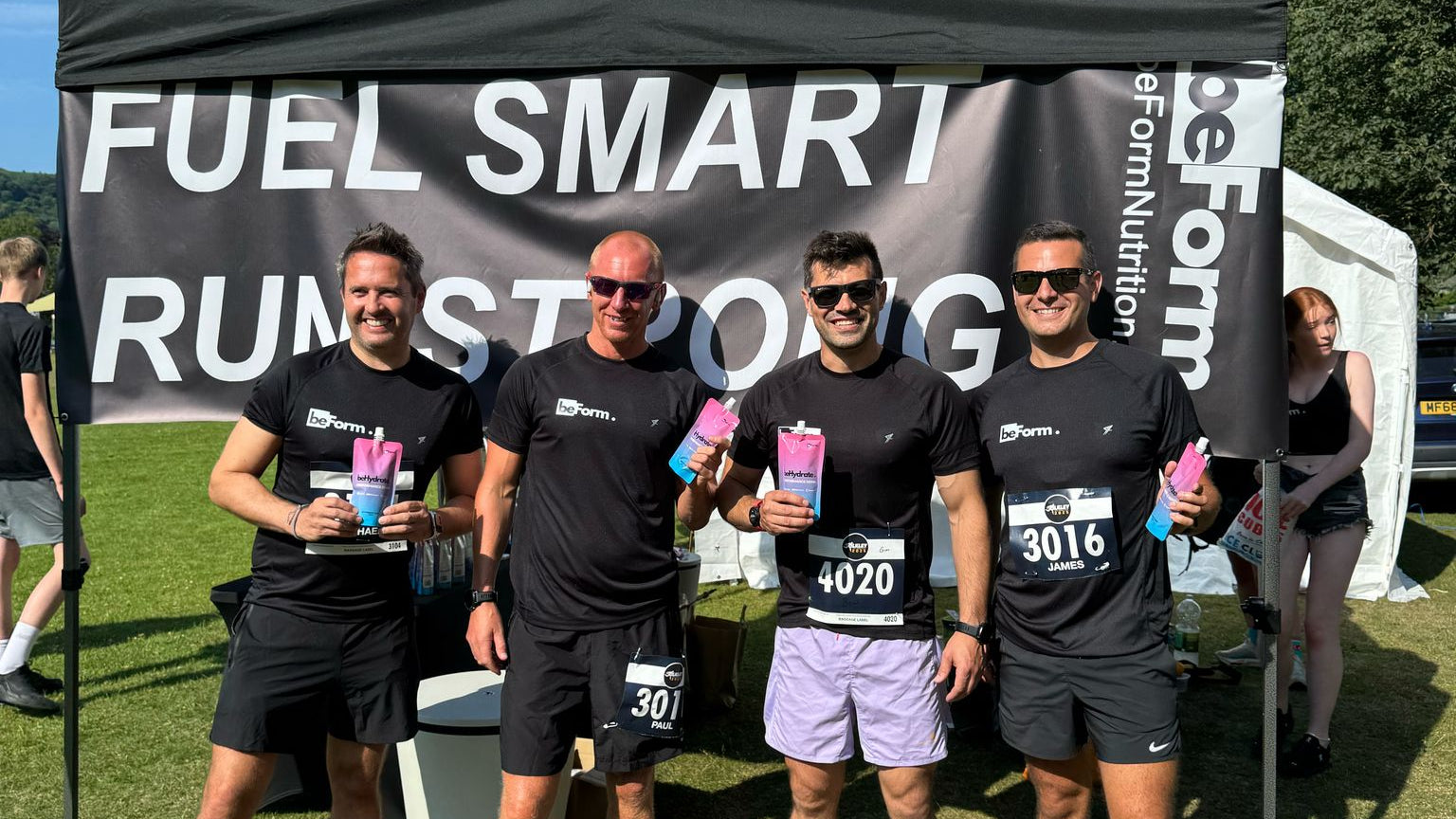 Four men in running gear standing in front of a beForm Nutrition 'Fuel Smart Run Strong' tent with a banner.