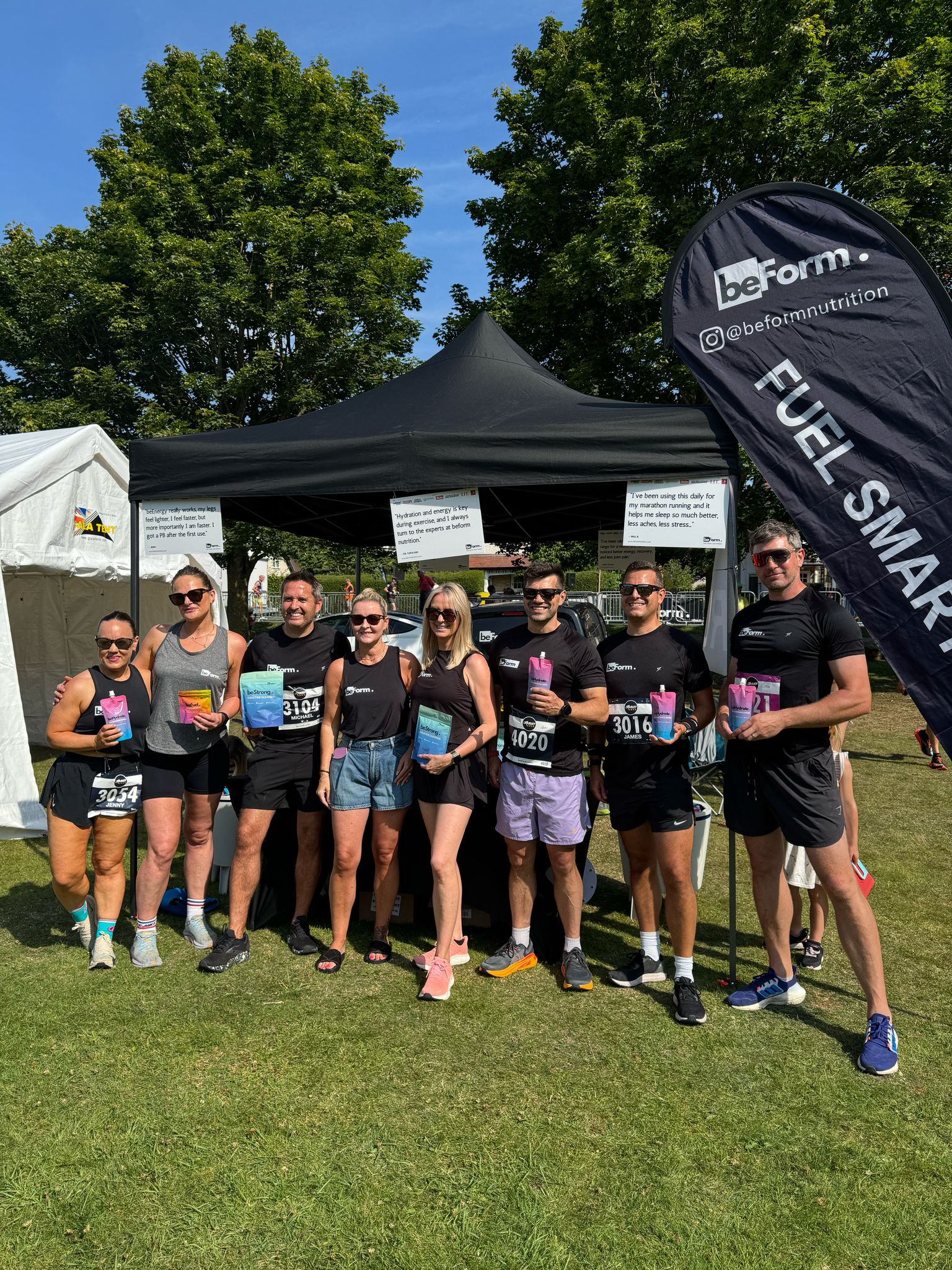 Group of people holding beForm Nutrition products in front of a tent with a visible brand logo.