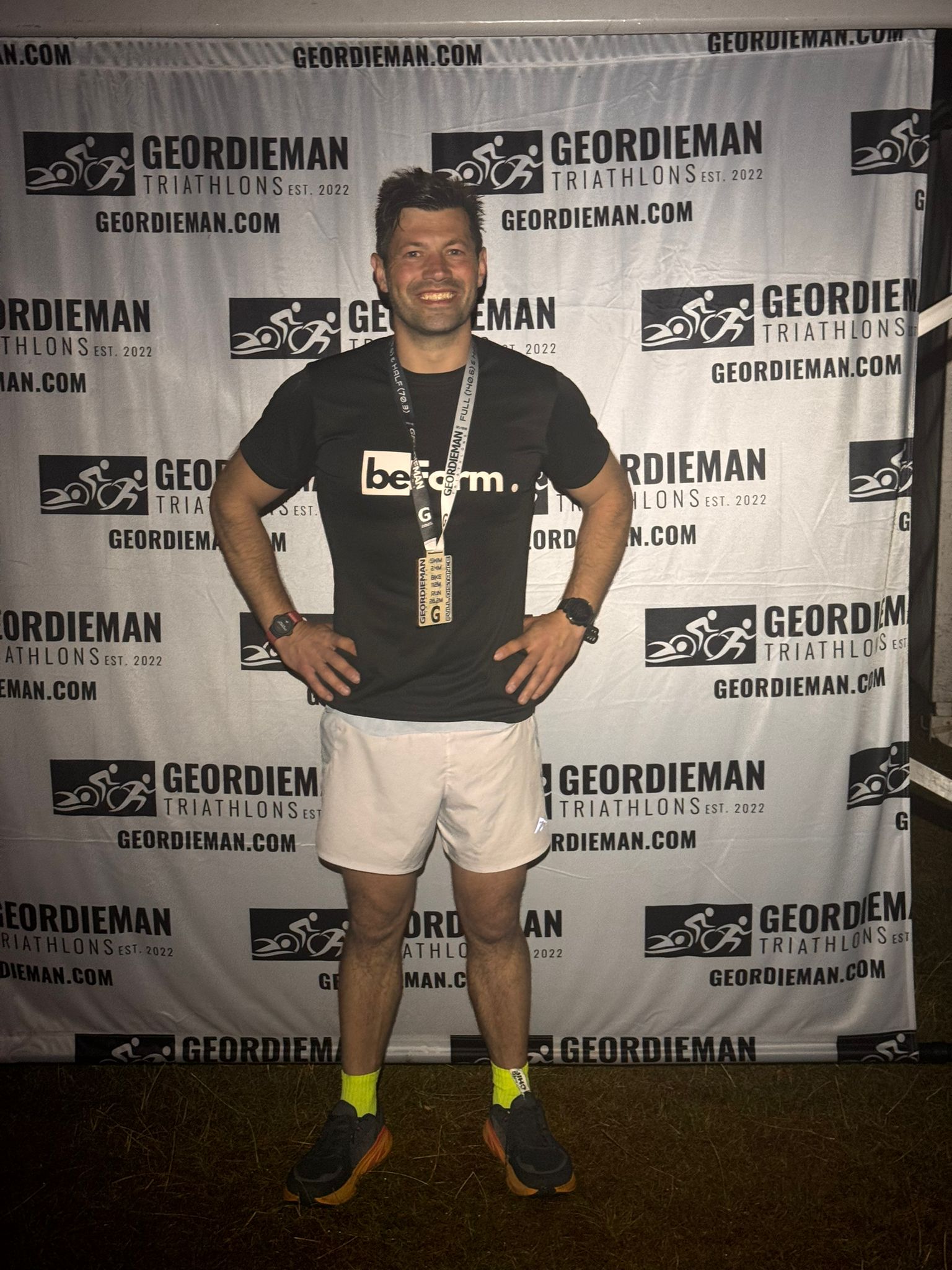 Man posing with a medal in front of a Geordieman Triathlons backdrop
