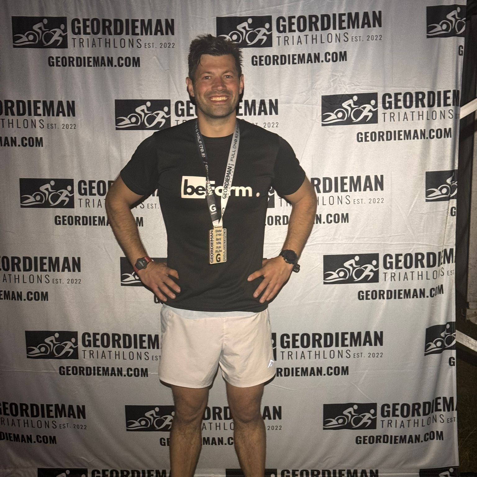 Man posing with a medal in front of a Geordieman Triathlons backdrop