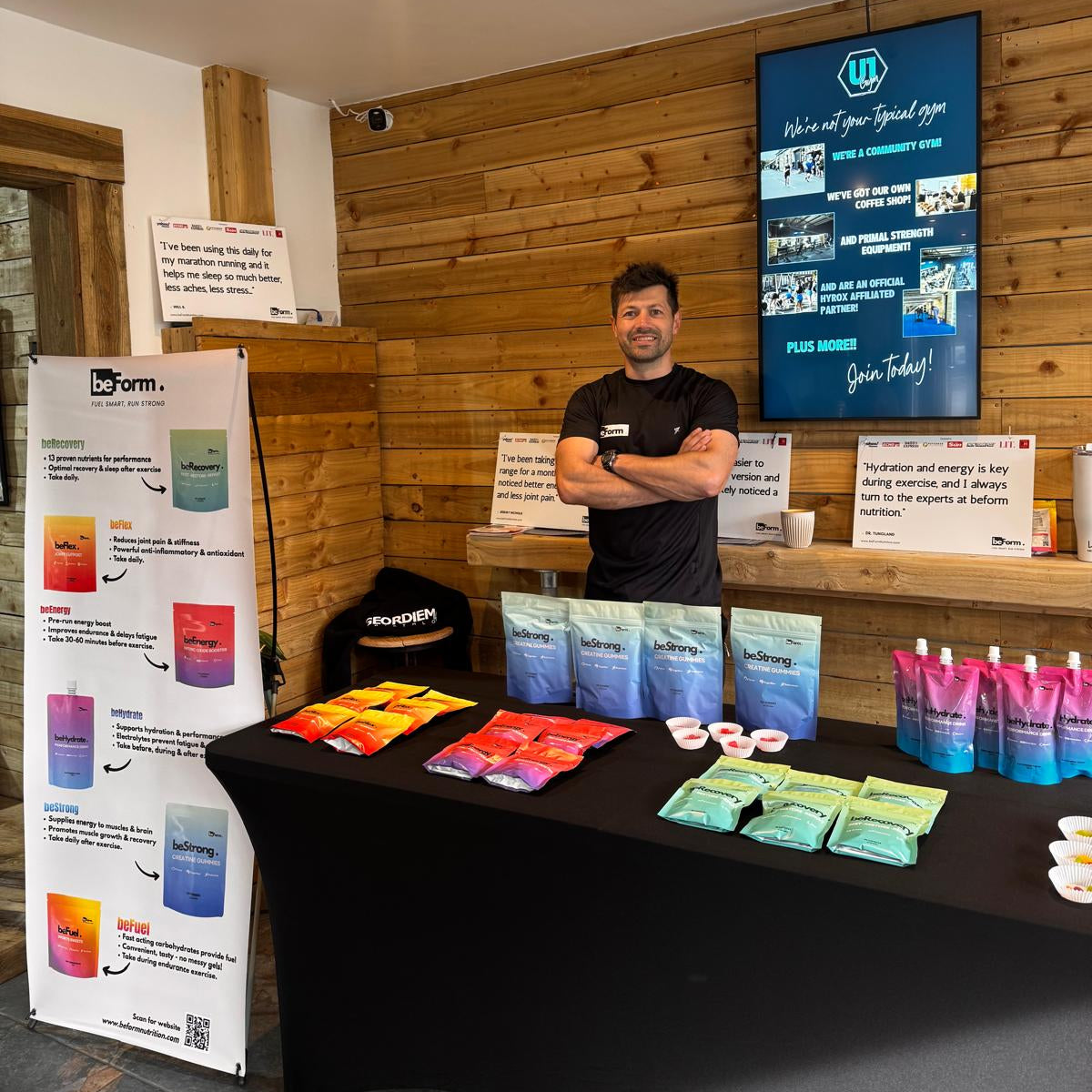 Man standing behind a table with packets of sports nutrition packets from beForm nutrition in a wooden interior of a gym setting