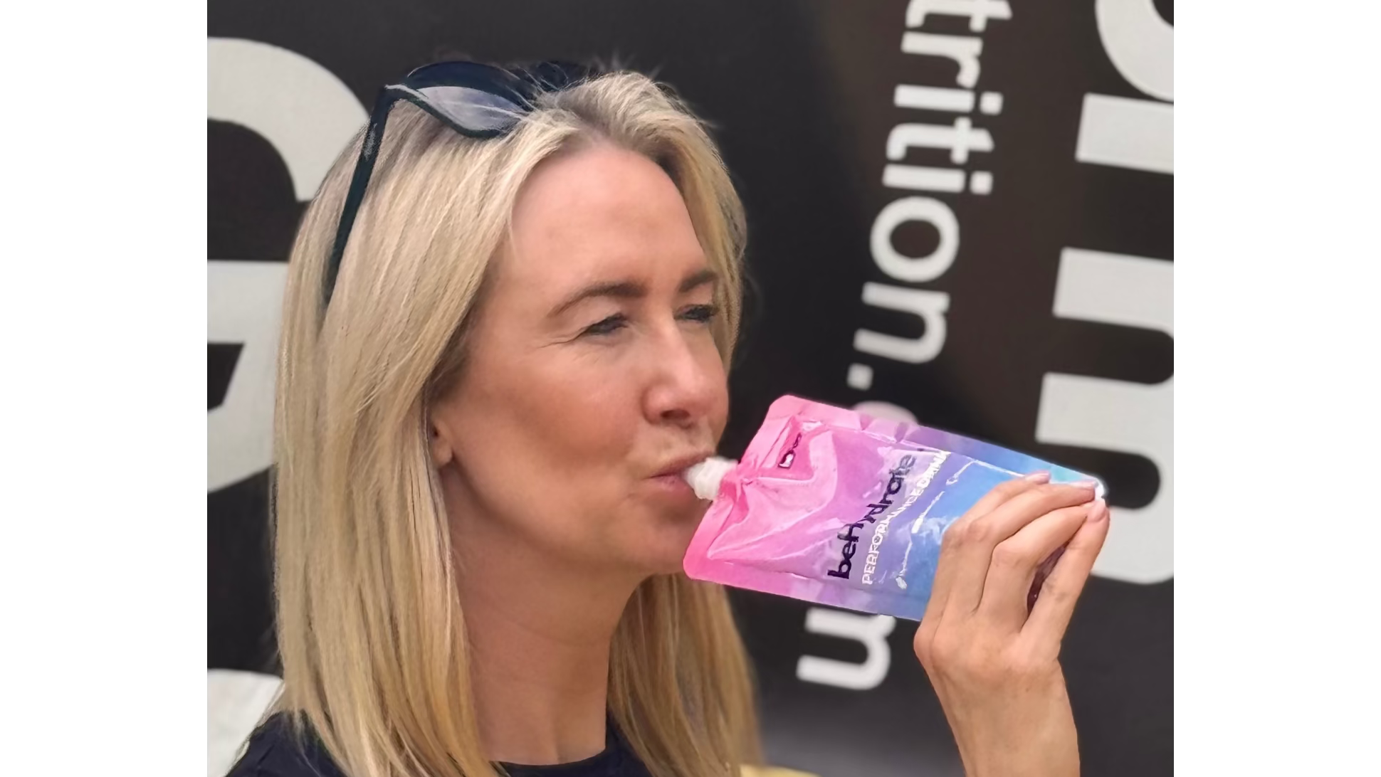 Woman drinking from a pink and blue beHydrate pouch with 'beform' branding in the background
