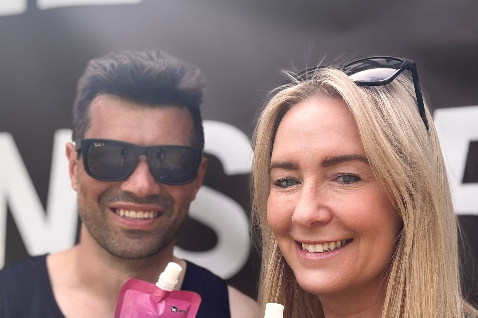 Two people holding behydrate performance drink pouches with a brand name in the background.