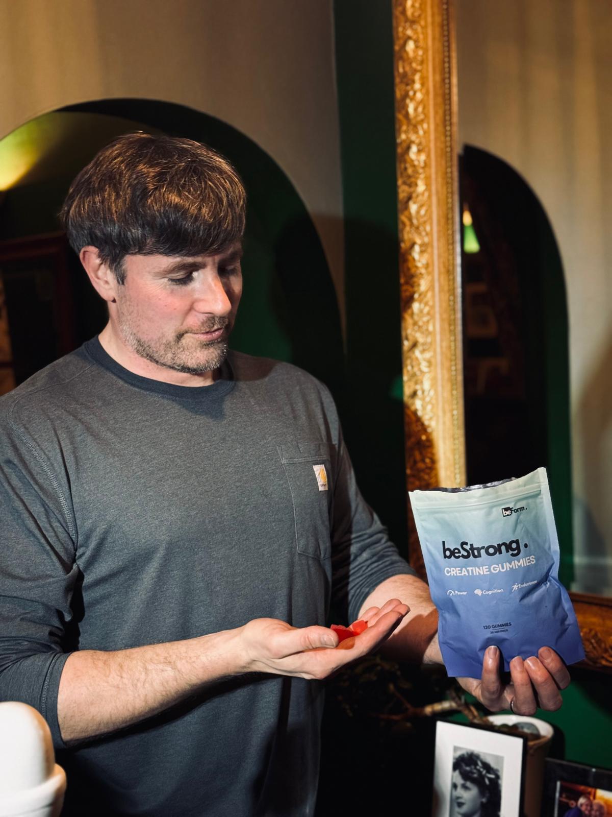 Man holding a blue 'beStrong' packet and red candies in a casual setting.
