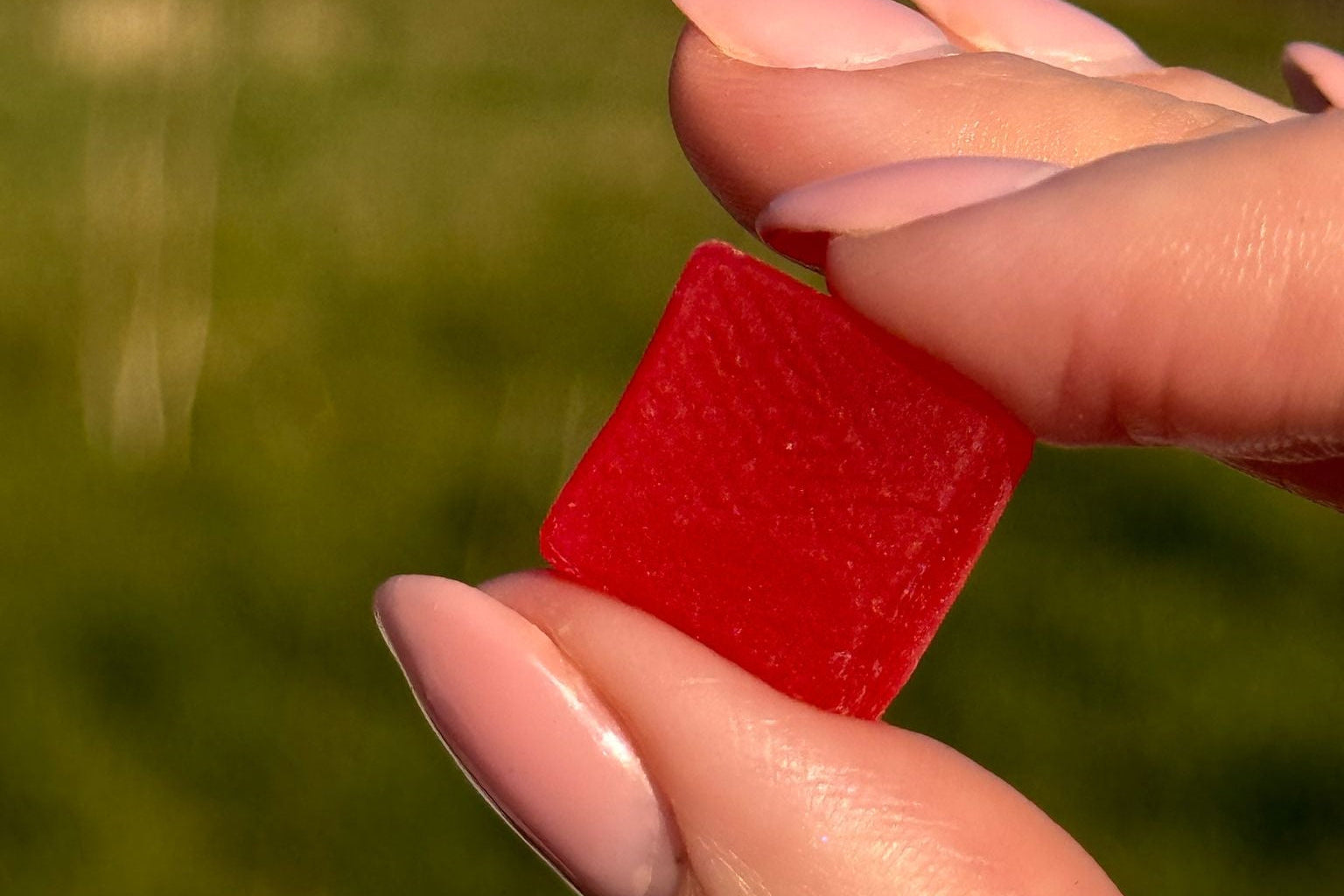 Red creatine gummy held by a hand with a blurred natural background