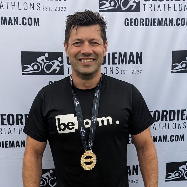 Man in beform nutrition athletic wear standing in front of a Geordieman Triathlon backdrop wearing a medal