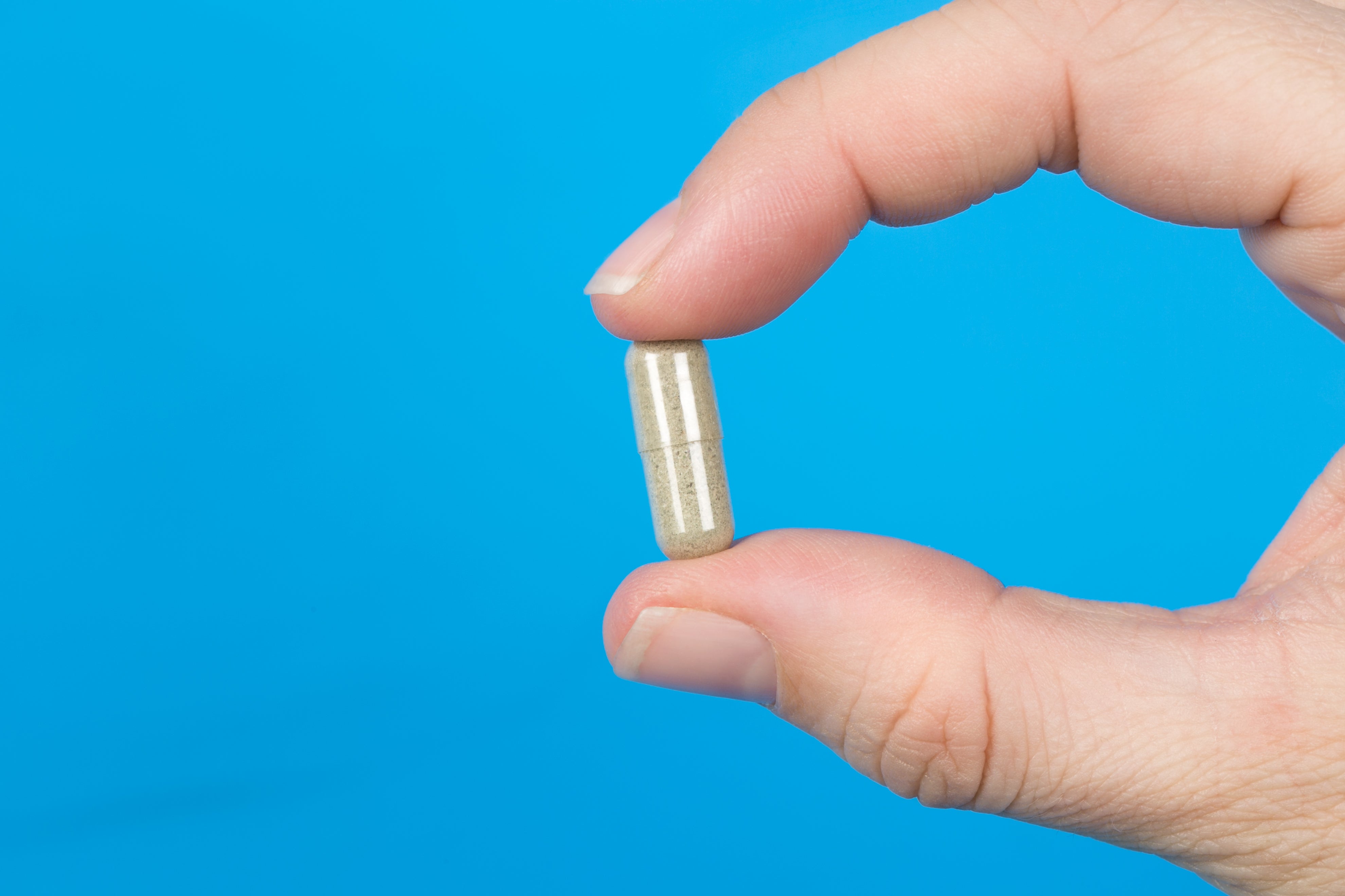 a hand holding a transparent supplement capsule with a vivid blue background.