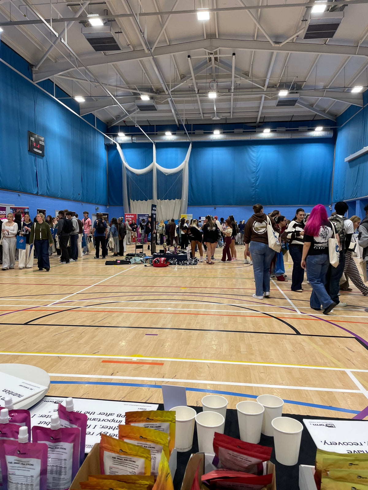 the interior of a sports hall with people and promotional stands