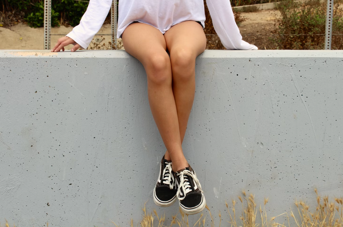 womans shins whilst she is sat on a wall and wearing Vans trainers