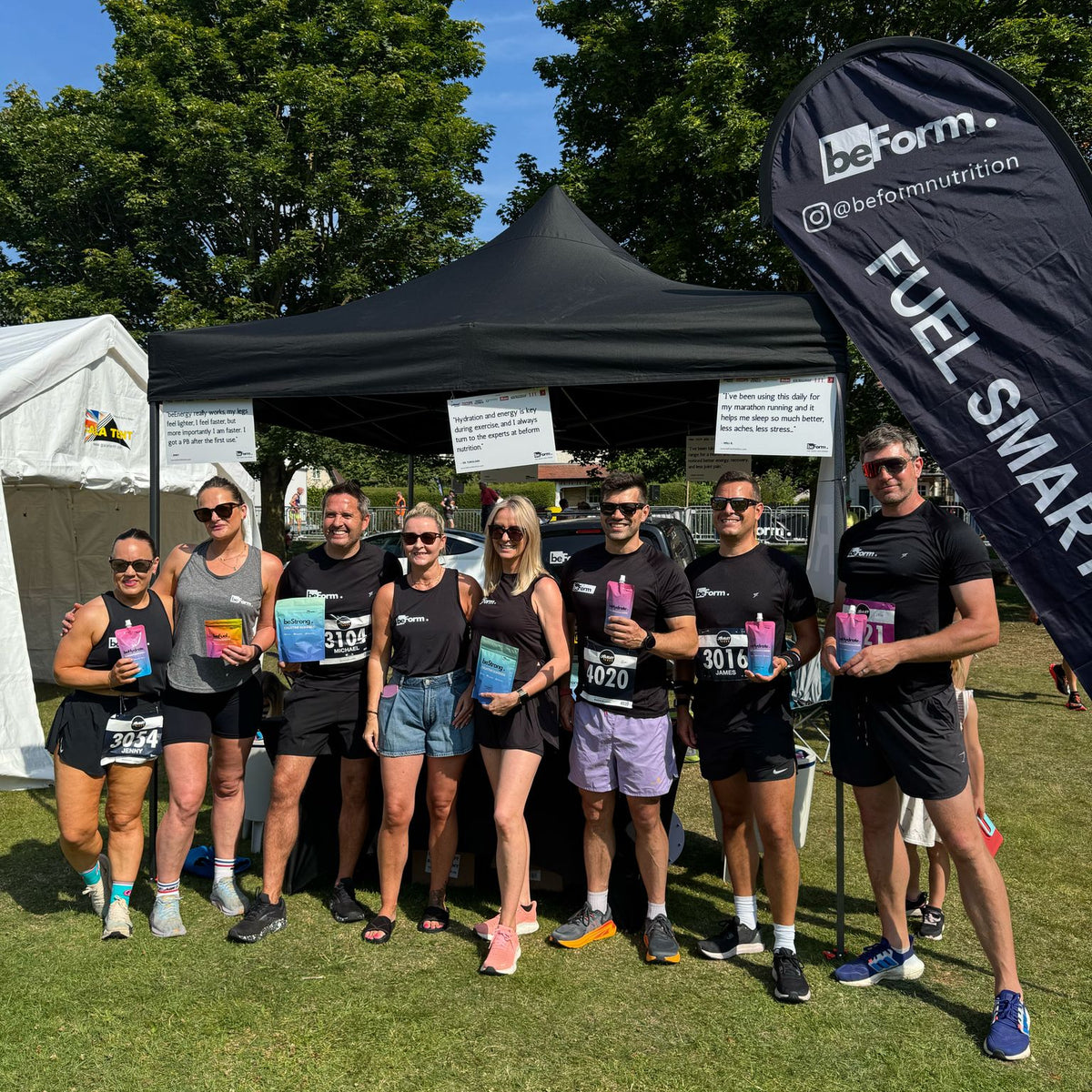 Group of people holding beForm Nutrition products in front of a tent with a visible brand logo.