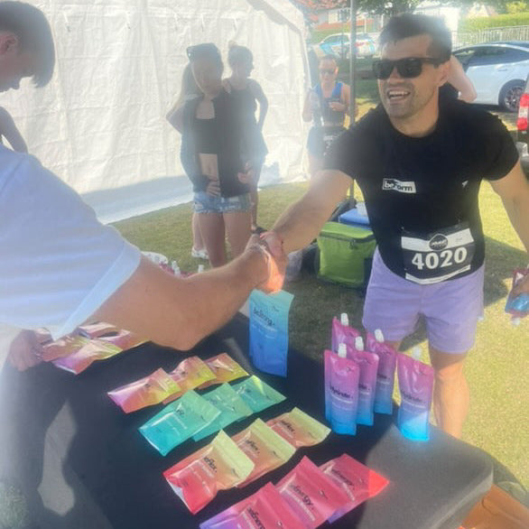Man in black t-shirt with race number 4020 shaking hands with another person at an outdoor event.