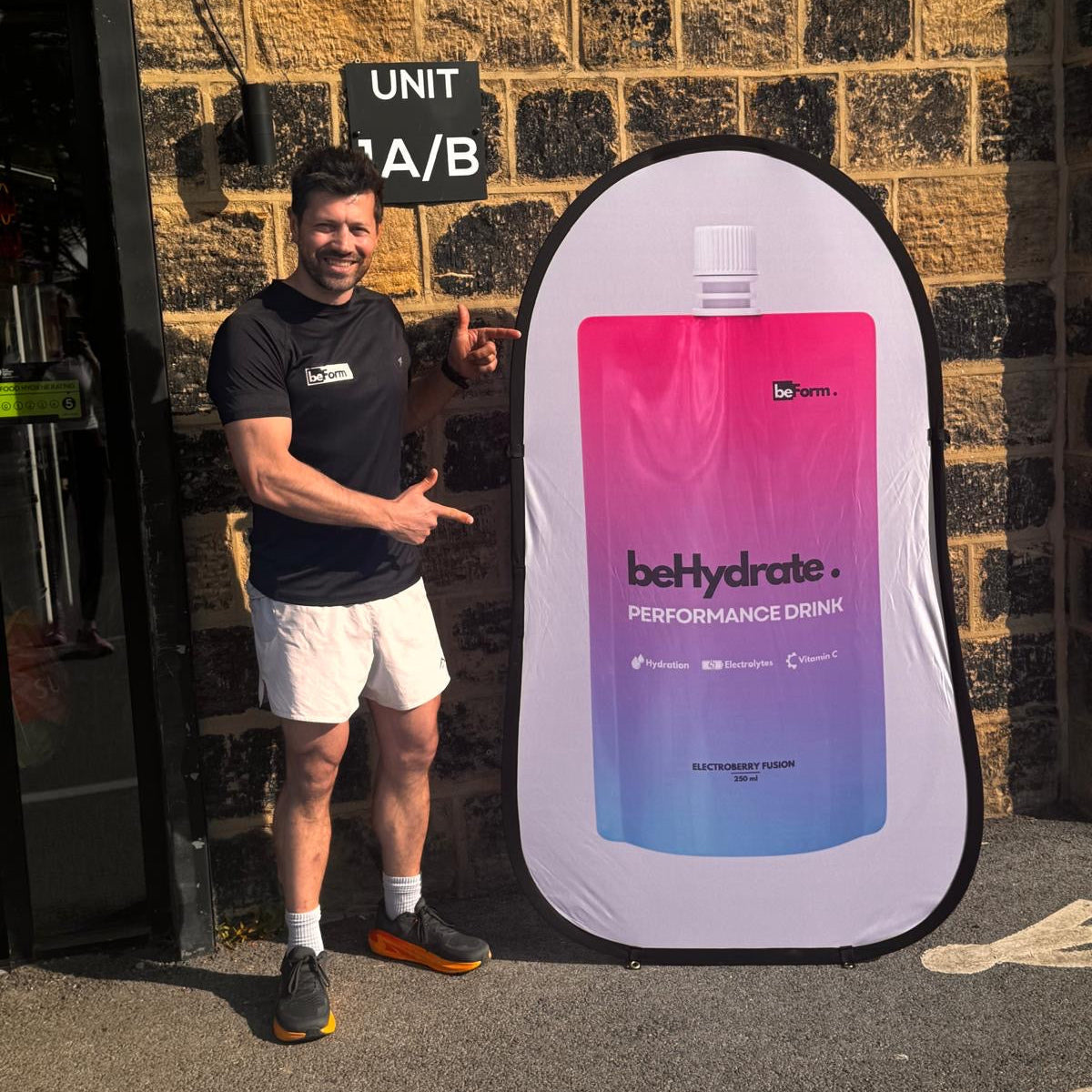 Man pointing at a large beHydrate performance drink container against a brick wall.