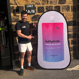Man pointing at a large beHydrate performance drink container against a brick wall.