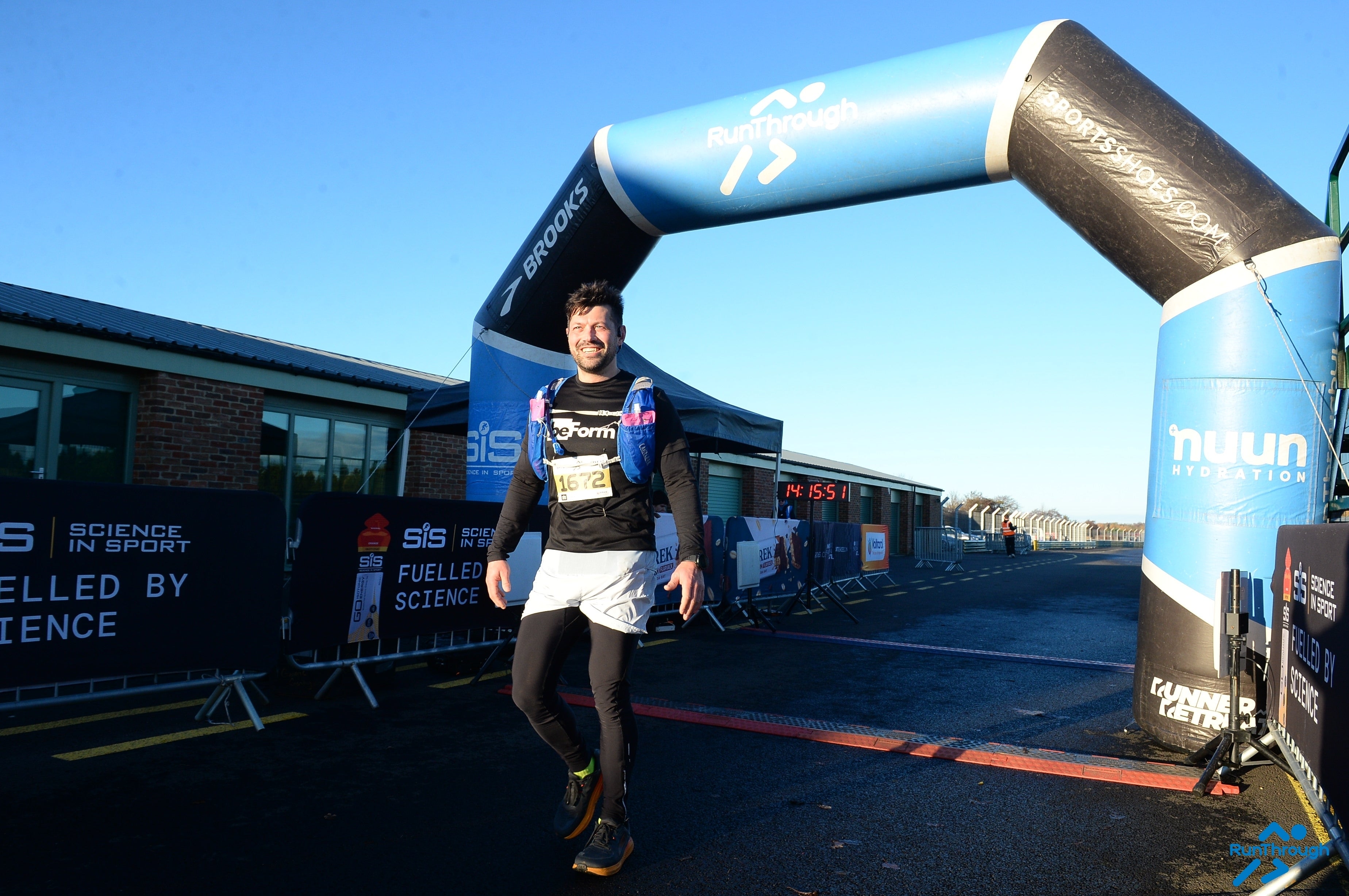 Person standing under a blue and black inflatable archway on the finish line of a marathon wearing a black long-sleeved tee shirt with the beform nutrition logo.