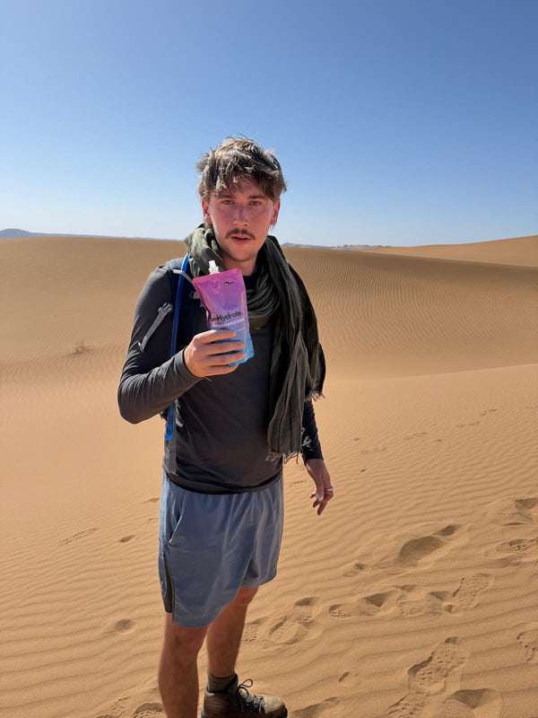 Person holding a piuch of beHydrate performance drink in a desert landscape