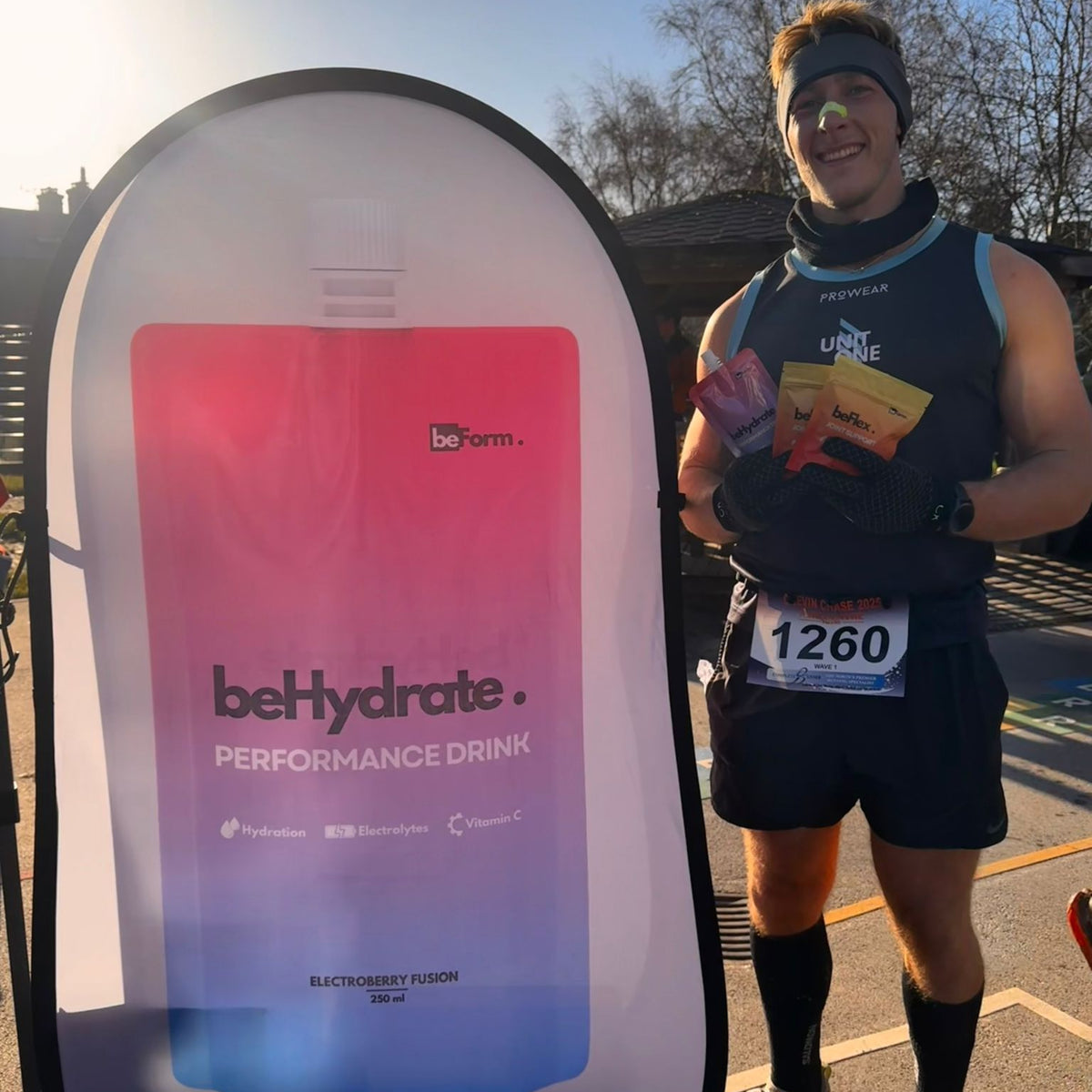 Person holding a behydrate performance drink container next to a large beHydrate sign at a running event