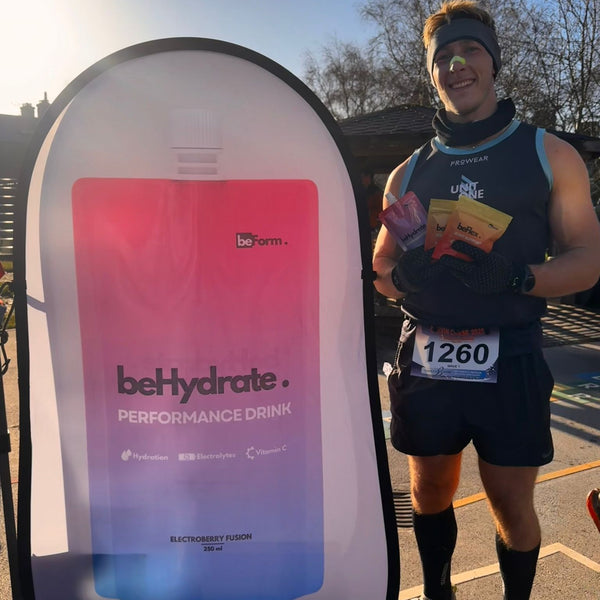Person holding a behydrate performance drink container next to a large beHydrate sign at a running event