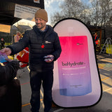 Man handing out a product in front of a behydrate promotional stand.