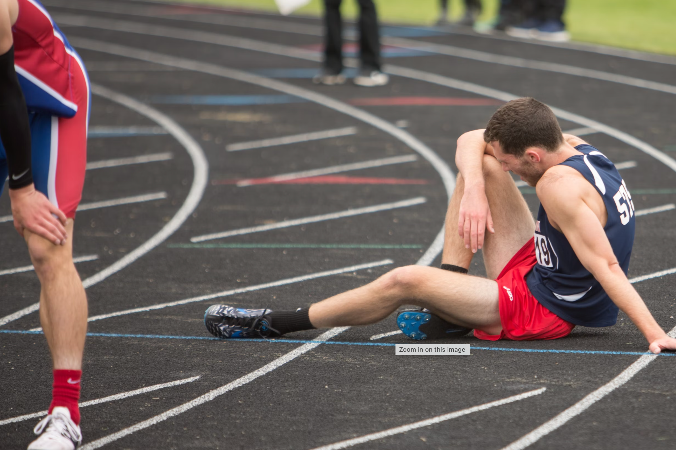 Exhausted Athlete slumped on a running track with another athlete in the foreground.