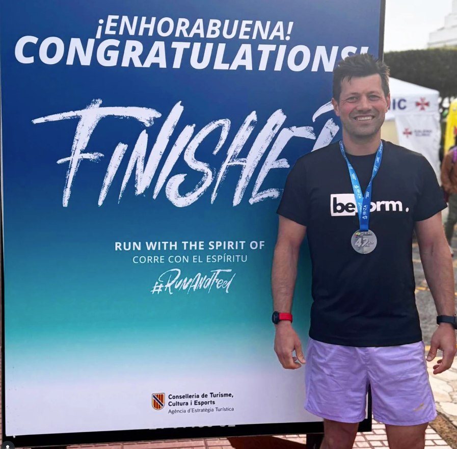 Man standing in front of a 'Congratulations Finisher' sign with a blue gradient background