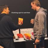 two men talking in front of a table with beform nutrition products in colourful packaging.