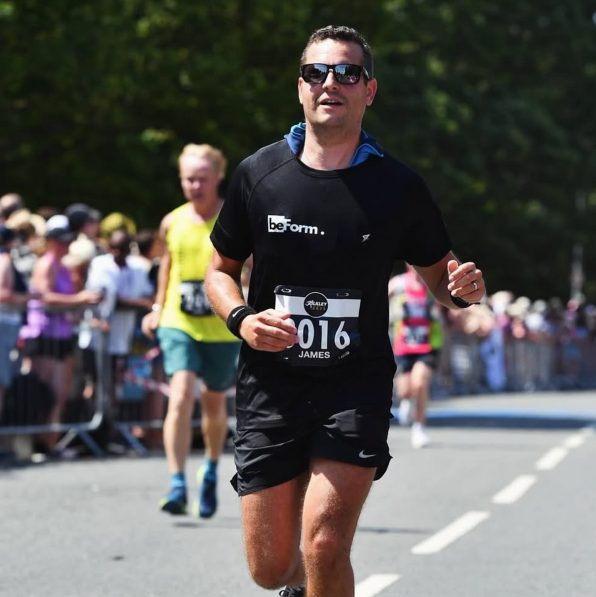 man with brown hair running at the ilkley half marathon wearing a running number bib and a black beform nutrition tee shirt.