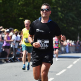 man with brown hair running at the ilkley half marathon wearing a running number bib and a black beform nutrition tee shirt.