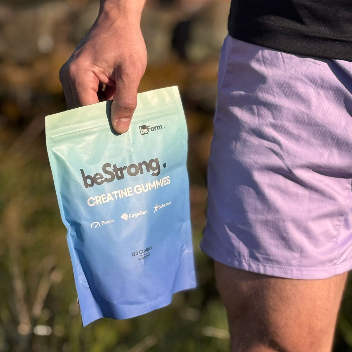 Person holding a blue package of 'beStrong' creatine gummies in a natural setting.