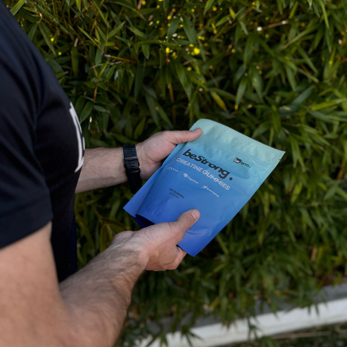 man holding a pack of bestrong creatine gummies infront of natural vegetation