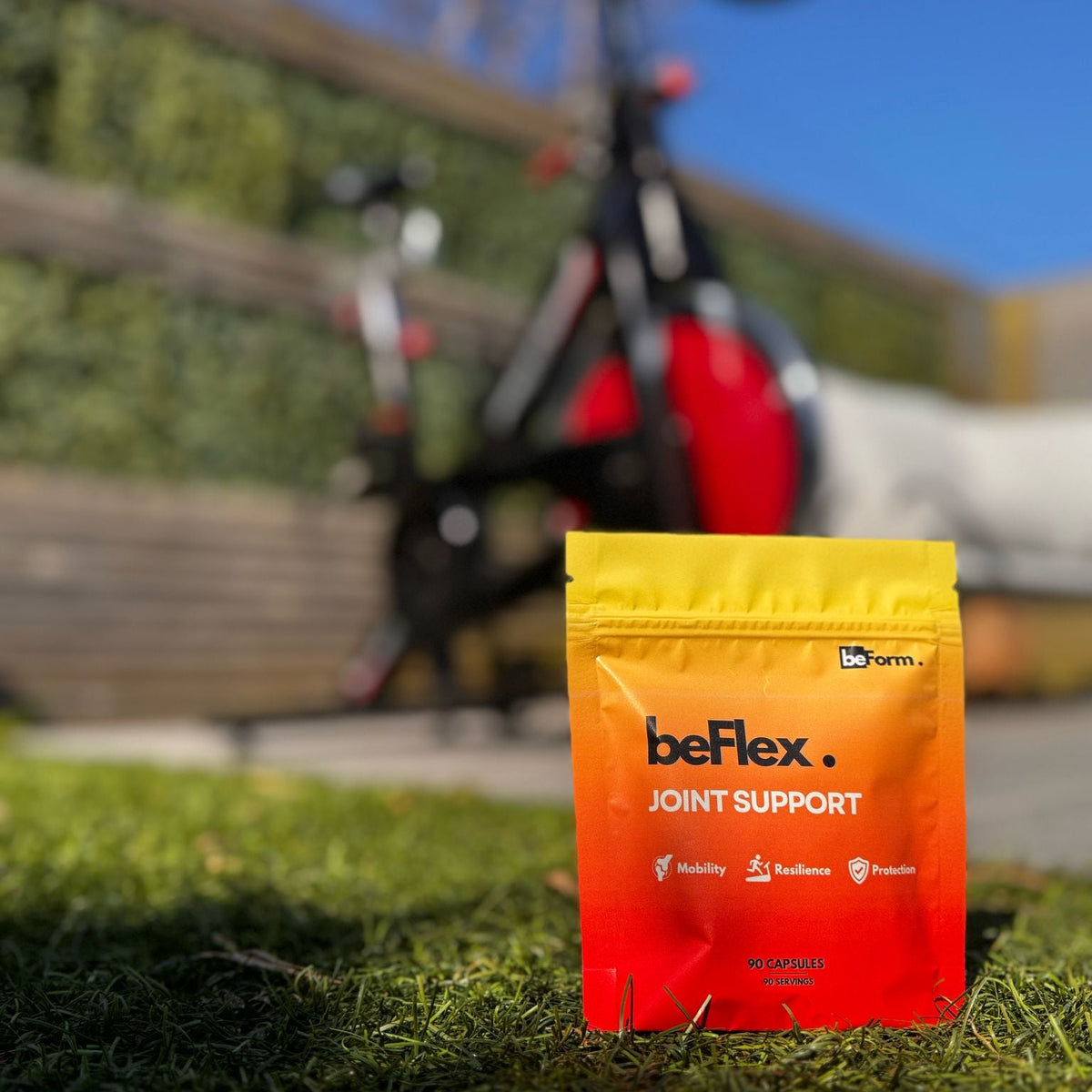 Orange and yellow packet of joint support supplement on grass with bicycle in background