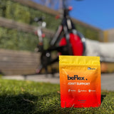 Orange and yellow packet of joint support supplement on grass with bicycle in background