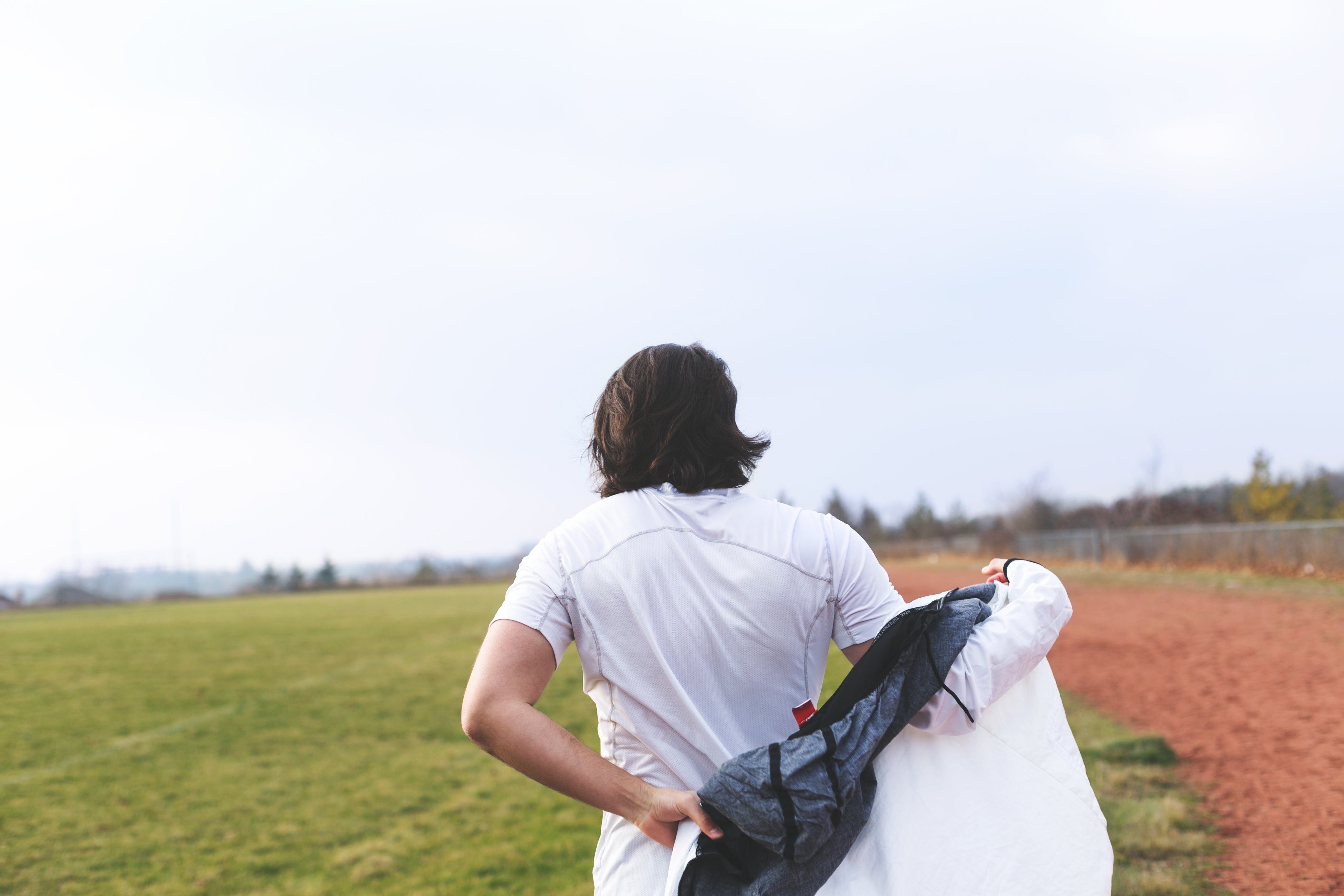 man with long brown hair putting on a jacket next to a running track.