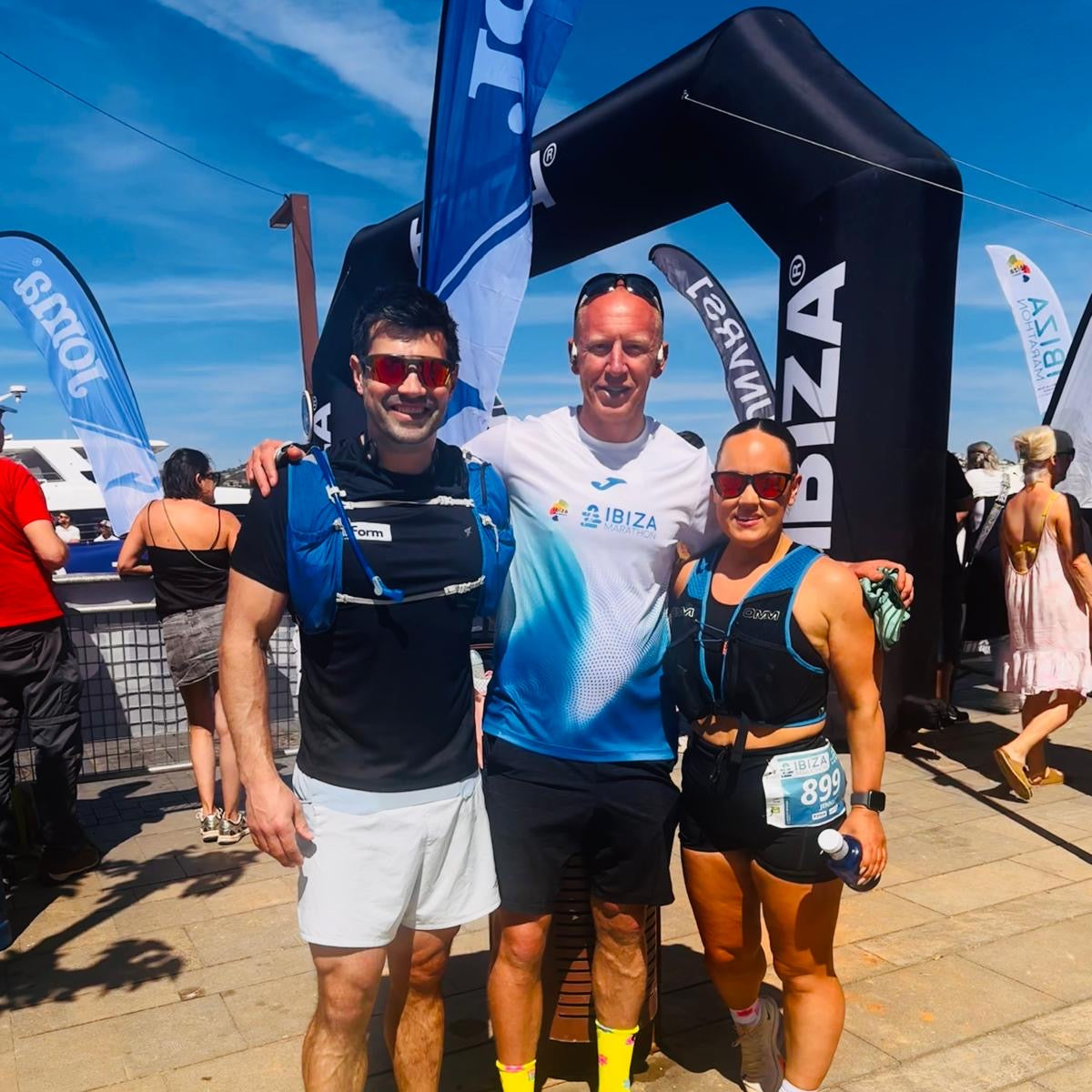 Three runners posing together at a race finish line with event branding in the background.