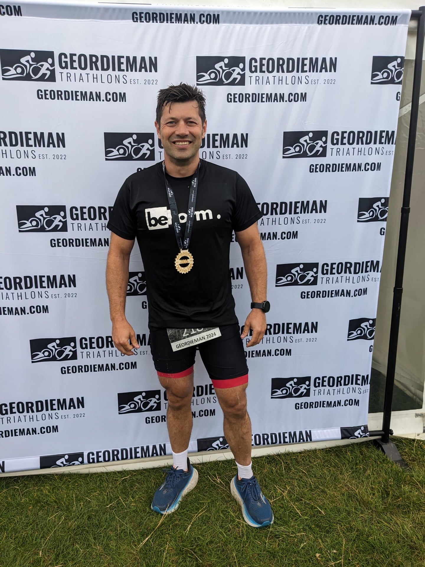 Man in athletic wear standing in front of a Geordieman Triathlon backdrop