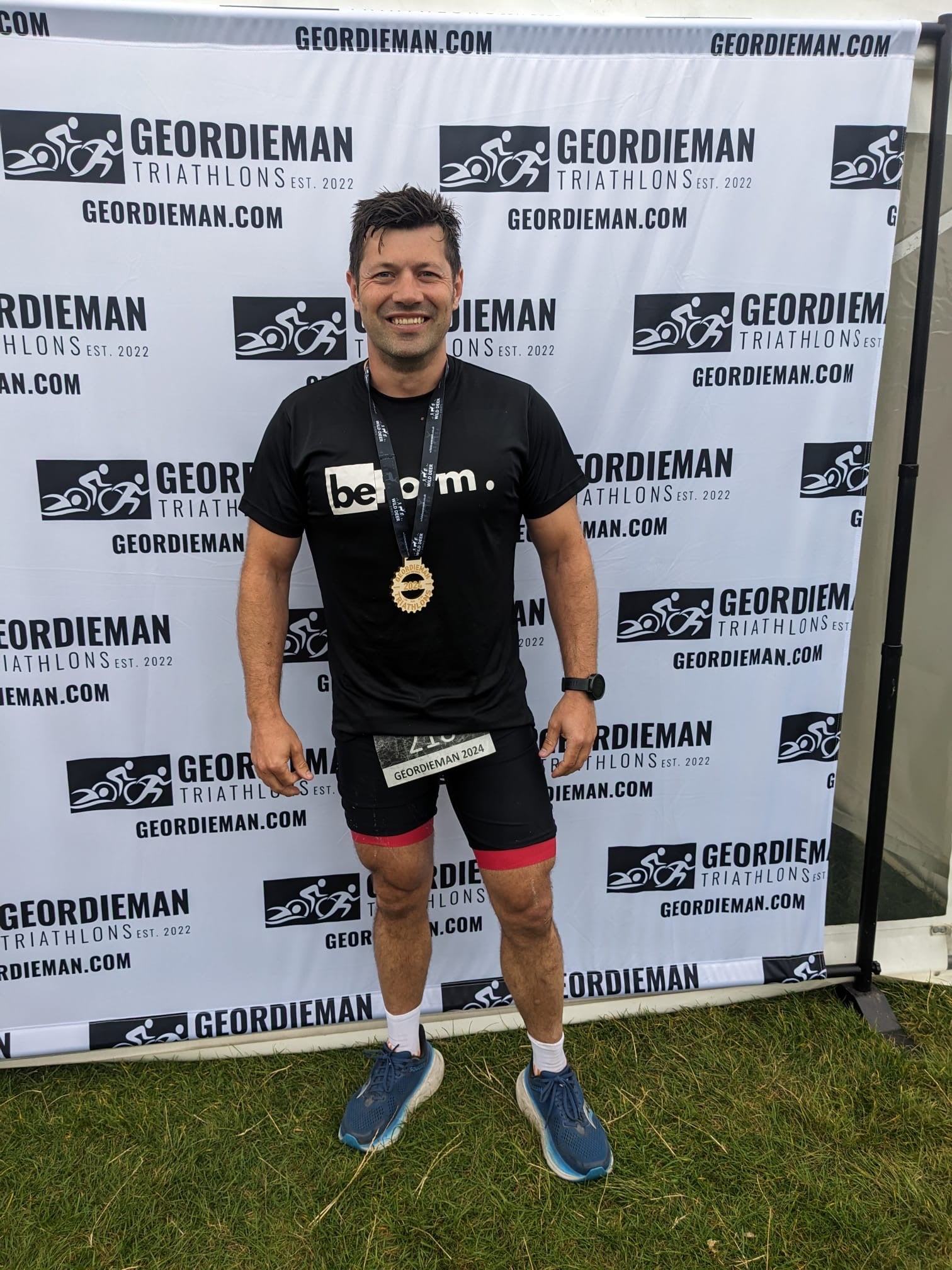 Man in athletic wear standing in front of a Geordieman Triathlon backdrop