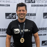 Man in beform nutrition athletic wear standing in front of a Geordieman Triathlon backdrop wearing a medal