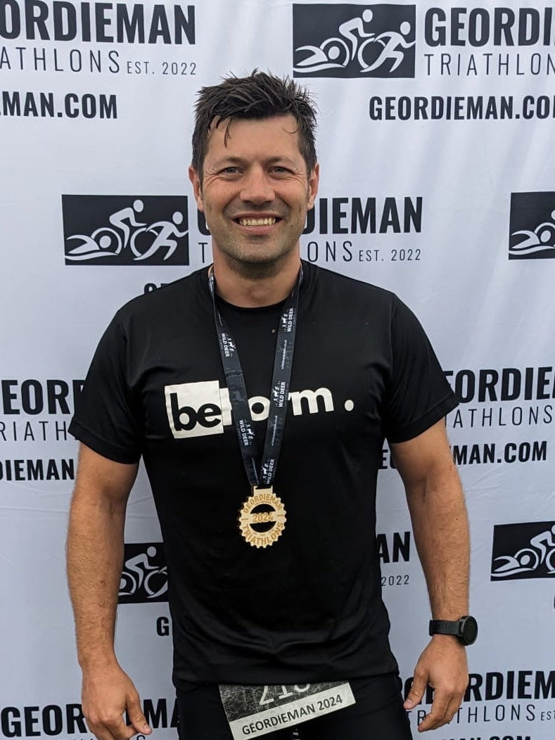 Man in athletic wear standing in front of a Geordieman Triathlon backdrop