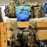Camouflage backpack with tactical equipment and a blue 'beStrong' packet on a wooden surface.