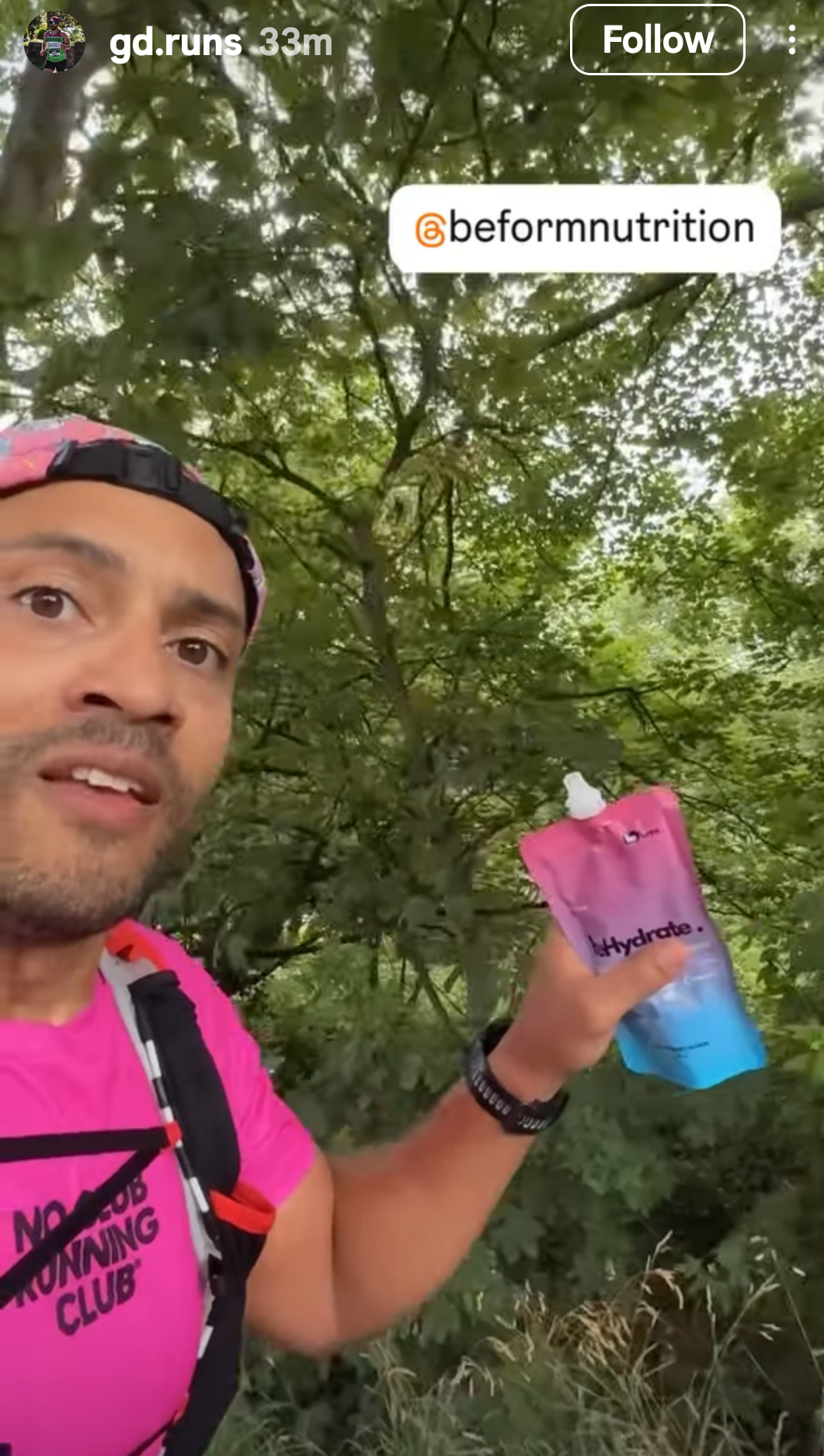 Person holding a pink behydrate performance drink pouch with trees in the background