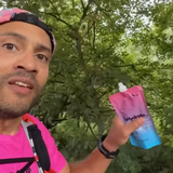 Person holding a pink behydrate performance drink pouch with trees in the background